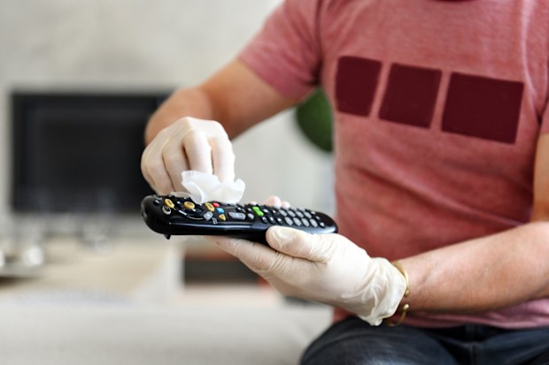 person wiping down remote control surfaces