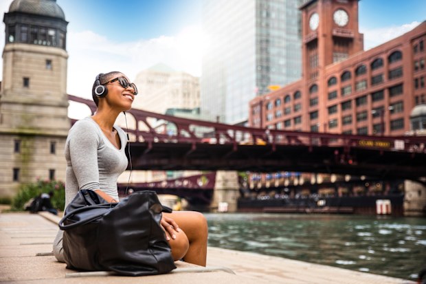 Woman in the city listening to music using wireless headphones.
