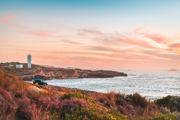 4WD car parked on rocky beach in Robe with driver enjoying the scenic sunset view with ocean, South Australia