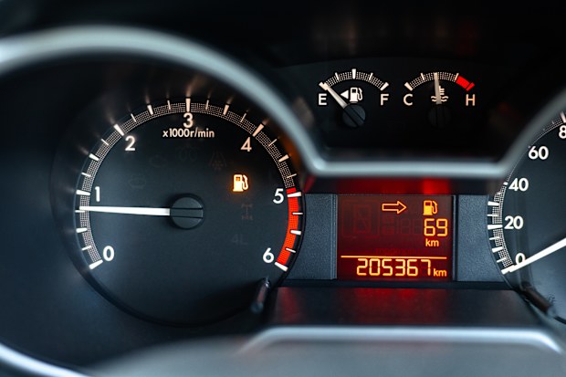 Close-up of a car dashboard showing a low fuel warning light and remaining distance display, representing fuel shortage, travel planning, vehicle awareness, and driving risk management.