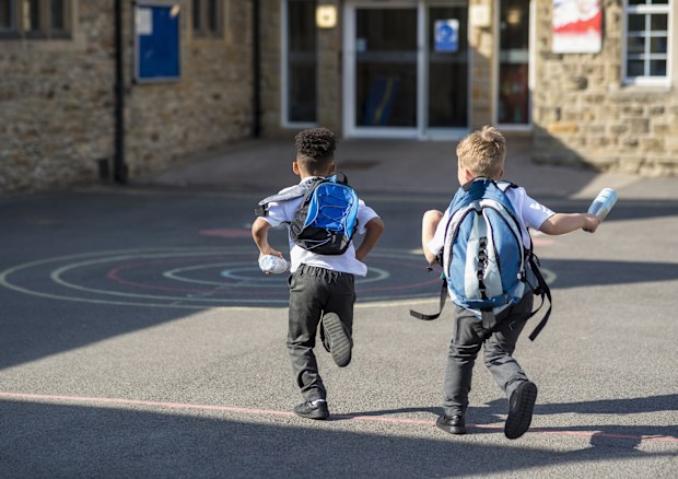 Rear view of two boys running in their school yard in uniform 