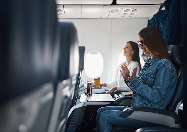 Female on passenger seat of plane clapping her hands with joy and laughing while staring at her laptop display