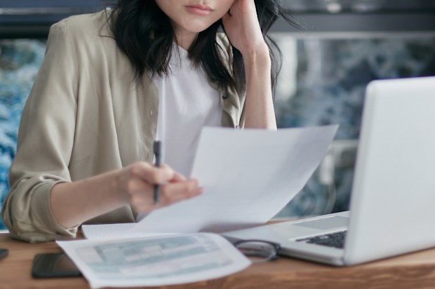 A woman looks worried about money while paying bills on a laptop. Stock photo.