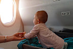 Happy infant baby lyes in special bassinet in airplane at his stomach. First flight of the baby, she is impressed and looking in the window of plane