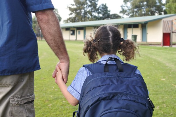 Rear view of schoolgirl holding her fathers hand on the way to school. Real people. Copy space