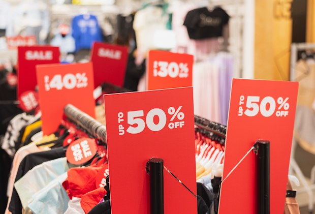 Red discount signs on clothes racks in a clothing store.