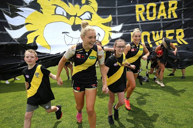 AFLW player Jess Hosking runs onto the field at her 50th game with two 'cleft kids'.