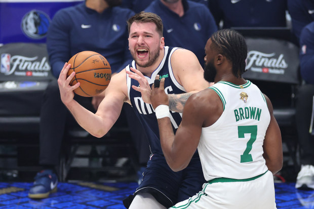 Luka Doncic of the Dallas Mavericks dribbles while being fouled by Jaylen Brown of the Boston Celtics.