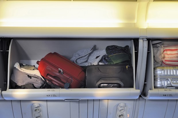 Carry-on luggage in overhead storage compartment on commercial airplane.