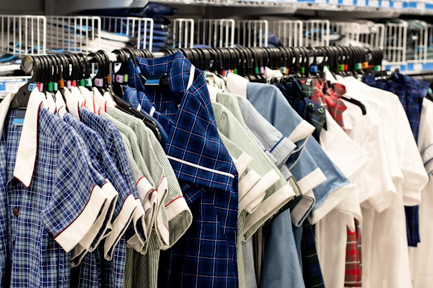 Various colors school uniform dresses for girls on hangers on the rack at the shop. 