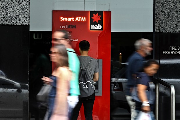 A man uses an NAB ATM as pedestrians walk past.