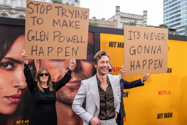 Glen Powell's parents hold up signs behind him as they attend the special screening of Hitman in Austin, Texas on May 15.