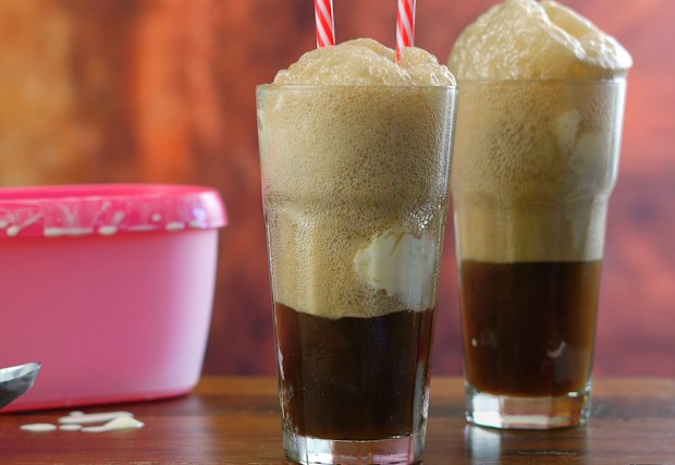 Preparing black cow cola ice cream soda floats against rustic wood background.