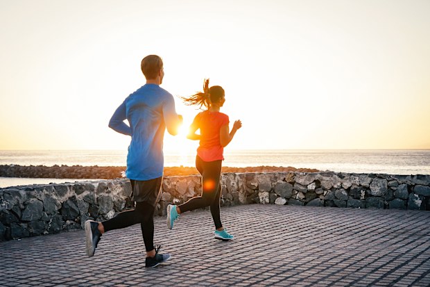 Health young couple jogging together next the ocean during a magnificent sunset - People work out on the beach - Relationship, sport, lifestyle concept