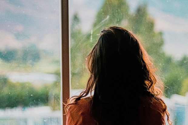 A woman looks out a window from behind. Stock photo.