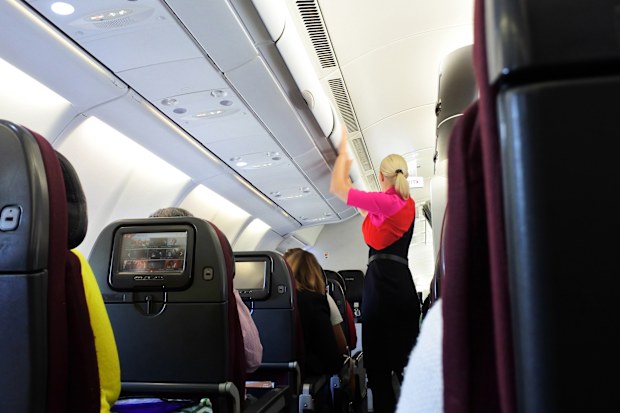 Qantas airways flight attendant closing the overhead luggage compartment inside a plane.