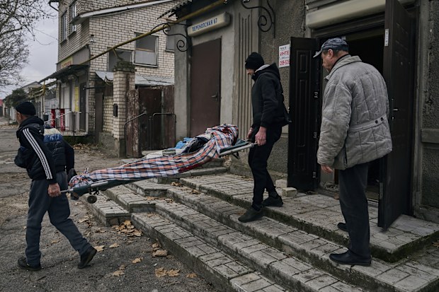 Local residents carry the body of a 20-year-old man killed in Russian shelling in Kherson, Ukraine, Thursday, Jan. 5, 2023. (AP Photo/LIBKOS)