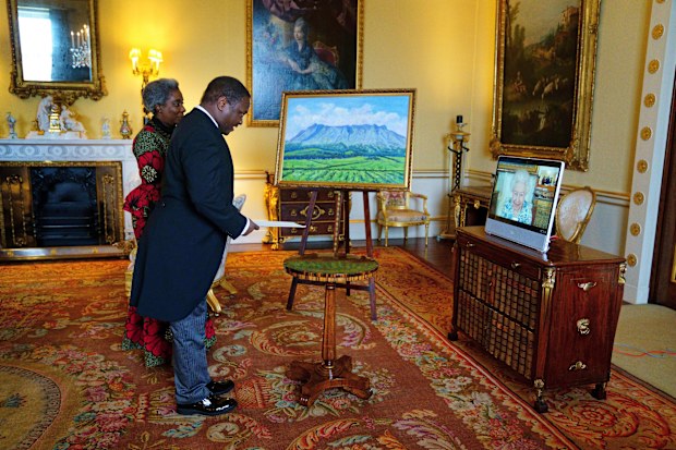 Queen Elizabeth appears on a screen via videolink from Windsor Castle, where she is in residence, during a virtual audience to receive the High Commissioner of Malawi, Dr. Thomas Bisika, centre, and his wife, at Buckingham Palace, London., Thursday, March 3, 2022. 