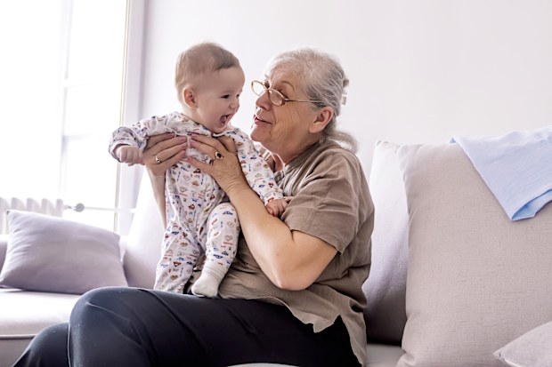 Grandmother holding little grandson in the room at home. Senior woman hold little baby cute smiling. Happy grandmother with her grandchild in home.