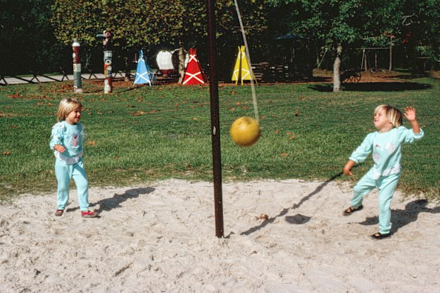 A horizontal image of two female children playing punchball on a playground on a sunny day.  There are no other children in the photograph and the ball is in motion.  Room for copy space