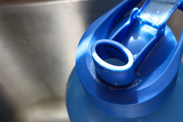 Cleaning a dirty reusable plastic water bottle in a kitchen sink