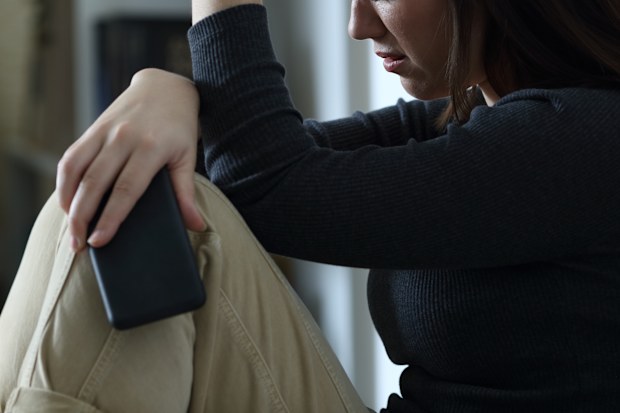 Sad woman holding smart phone complaining at home