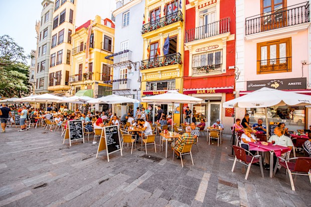 VALENCIA, SPAIN - August 19, 2017: Colorful buildings with cafes and restaurants crowded with tourists near the food market in Valencia city, Spain