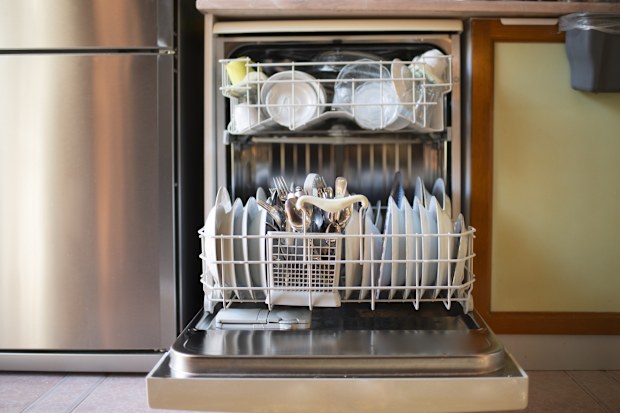 Housewife placing dishes in the dishwasher. Hand or machine dishwashing. Close up shot of modern housewife taking out clean dishes from dishwasher machine.