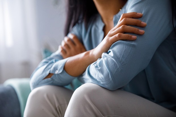 Midsection of unrecognizable young woman hugging herself to comfort while feeling sad and anxious.