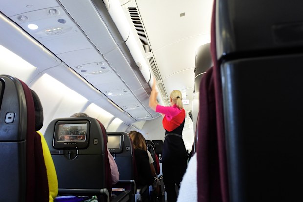 Qantas airways flight attendant closing the overhead luggage compartment inside a plane.