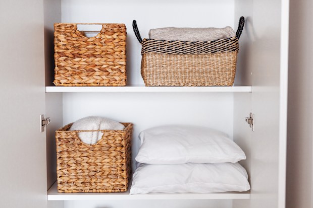 Laundry, pillows, towels organized and folded in wicker baskets on shelves in white wardrobe. Space organization and storage system. Tidy up closet