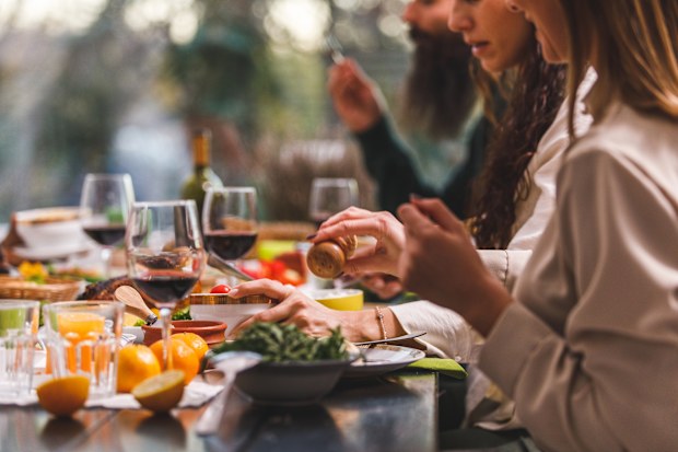 Copy space shot of young woman sitting at dining table with friends, adding salt to her meal she is enjoying for Christmas.