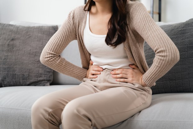The woman with a stomachache is holding her stomach in pain, sitting on the sofa in the living room. she is suffering from a stomachache. Healthcare and medical concept.