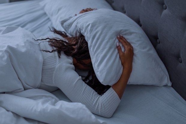 Sleeping Problem. Stressed African American lady lying alone in bed covering head under pillow feeling afraid or depressed, suffering from insomnia or mental problems after breakup