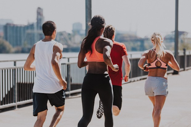 A biracial group of young adult athletes participating in a group workout, jogging down a city pathway on the Willamette River in Portland, Oregon.