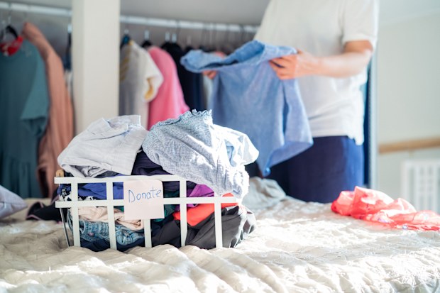 A Woman selecting clothes from her wardrobe for donating to a Charity shop. Decluttering Clothes, Sorting, And Cleaning Up. 