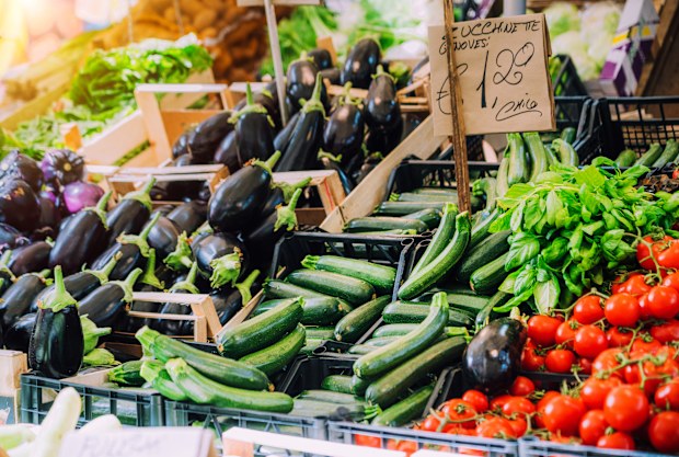 A colorful assortment of fresh vegetables including zucchinis, eggplants, and tomatoes showcased at a vibrant market stall in Sicily, Italy, embodying the region's dedication to fresh local produce.