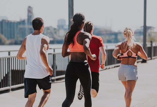 A biracial group of young adult athletes participating in a group workout, jogging down a city pathway on the Willamette River in Portland, Oregon.