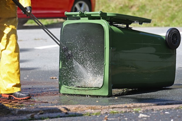 Sanitation worker uses a power washer to clean a compost recycling green bin.