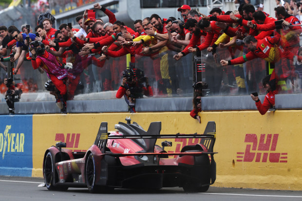 The race winning Ferrari 499P of Alessandro Pier Guidi, James Calado, and Antonio Giovinazzi passes the celebrating team on the pit wall at the finish of the Hours of Le Mans.