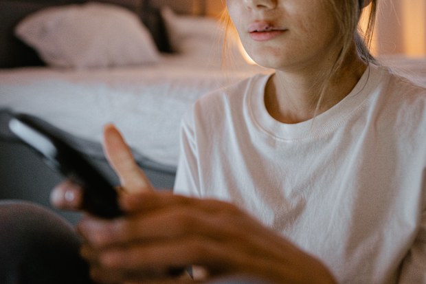 Woman with bruises and a split lip looks at her phone.