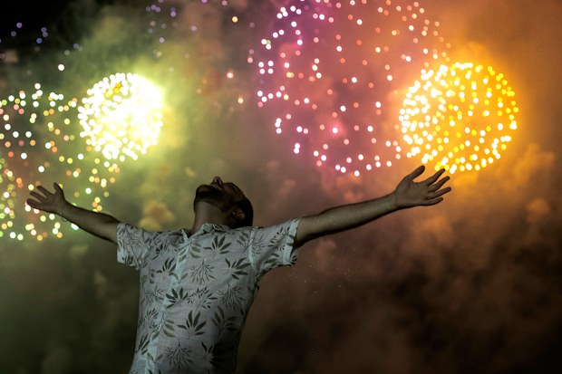 A man celebrates the start of the New Year, backdropped by fireworks exploding in the background over Copacabana Beach in Rio de Janeiro, Brazil, Saturday, Jan. 1, 2022.