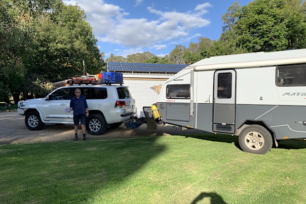 A man stands in front of a car attached to a caravan.