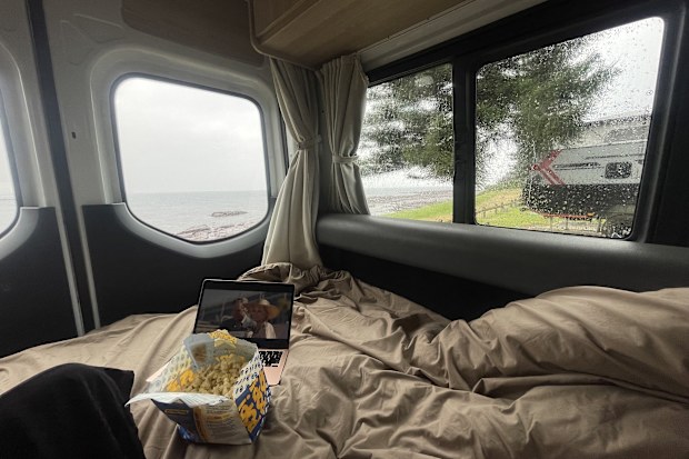 The interior of a campervan with a laptop and popcon bag sitting on the bed.