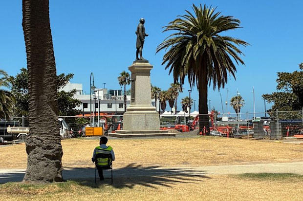 A security guard watches over a memorial to Captain James Cook in St Kilda on Australia Day after it was toppled by vandals two years ago. 26th January, 2026. Photo Rachael Ward.
