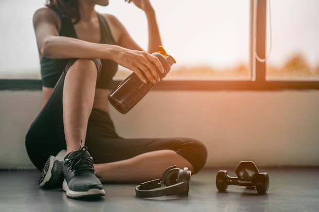Woman relaxing after exercise with a whey protein and dumbbell placed beside the gym.