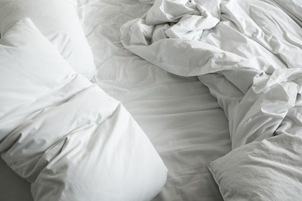 Unmade bed with white pillow, flat sheet, top sheet and quilt