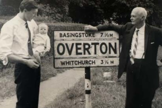 Peter Overton as a baby, being held by his father, as his grandfather looks on at the sign for the village of Overton in England.
