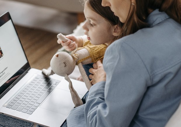 Working mum sits on her laptop with her child. Stock photo.