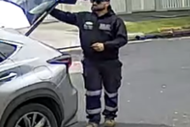 He was wearing a black hat, dark sunglasses, black "nina Pasadena" brand hoodie, blue work pants with prominent reflective strips and brown work boots.